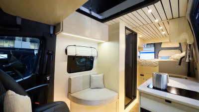 The Scandivans Sprinter 907 MWB L2H2 has wooden flooring.  The upholstery is cream and the driver’s seat is black.  The cabinets are wooden and the interior doors are black.  There is fixed rear bed.  Its rising roof is open.  