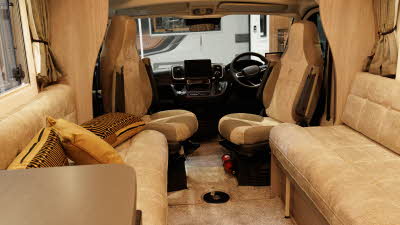 The Auto-Sleeper Nuevo EK Plus has cream upholstery, with the front two seats having tan leather panels.  These seats are swivelled to face inwards.  There is beige removable carpet on the floor. 