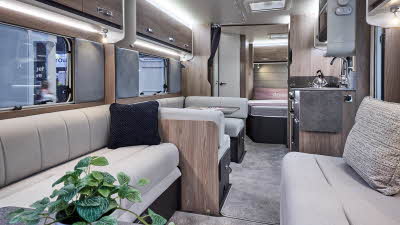 Interior of the Swift Challenger Grande 640 with beige sofas, cosy cushions and beige carpets.  There is a plant at the front.  The large windows and two sky lights will let natural light flood in.  The dinette is opposite the kitchen.