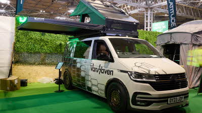 The Latitude Tents Explorer is displayed on a cream Volkswagen campervan.  It has green canvas and a hard top roof.  It has an extended platform.