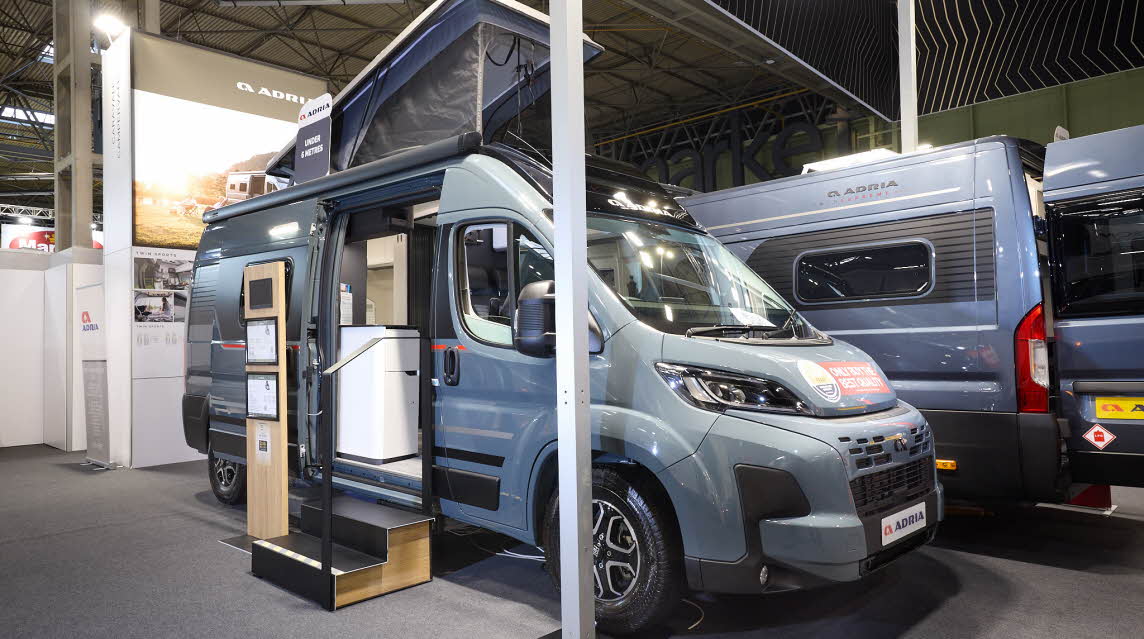 The Adria Twin Sport has a grey exterior.  The habitation door is open and there are two steps to gain easy access. There is an information board to the left of the steps.  The rising roof is open.