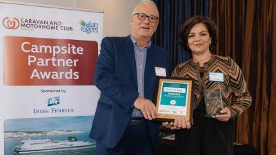 A Caravan and Motorhome Overseas Campsites Award Winner with the Chairman next to a sign showing Campsite Partner Awards, with Irish Ferries below it