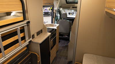 The Bailey Endeavour B65's rear is showing the rear bed in the lifted position.  The cabinets are made from pale wood.