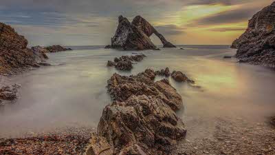 The peaks of Bow Fiddle Rock rising out in the distance with what looks like mist surrounding the rocky formations in the foreground