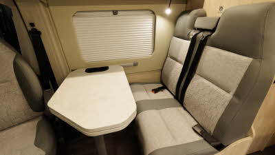 The Auto-Trail Expedition 68 XL Flex has brown and cream upholstery.  The drivers seat is swivelled into the centre of the van, there is a marble effect extending table between the three chairs.
