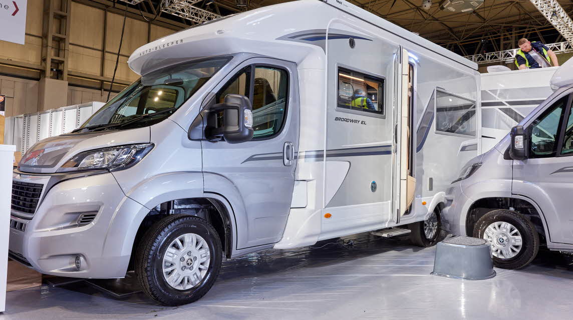 Auto-Sleeper Broadway EL exterior, the motorhome is silver and white, the rear habitation door is open showing into the interior, with a step to gain easy access. 