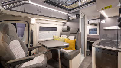 Adria Twin Supreme's interior has brown and beige upholstery with three yellow cushions, there is a large clear sunroof and the front passenger's seat is swivelled.  The fixed bed is to the rear with the hob on the right hand side.