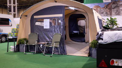 The Trigano Camplair S has yellow canvas with a brown canvas front. The exterior door is open. There are two camping chairs outside the tent.