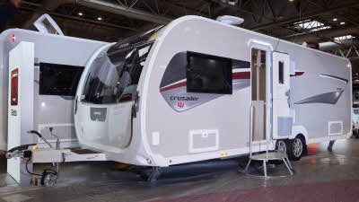 Elddis Crusader Zephyr’s exterior is grey with a grey and dark red patterned decal.  The entrance door is open and there is a large metal step to gain easy access.  The roof light is open and there is a TV aerial on the roof.