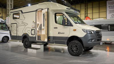 Eura Mobil Xtura XT’s exterior has cream body with grey large bumpers and rocker panels.  It has black patterned decals.  The habitation door is open and there are two steps to gain easy access.  The two large skylights are open. 