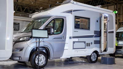 Auto-Sleeper Nuevo EK exterior, the motorhome is silver and white, the rear habitation door is open showing into the interior, with a step to gain easy access.  The two roof lights are fully open.