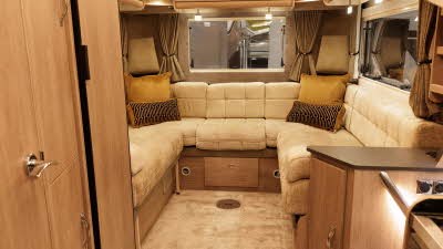 The Auto-Sleeper Broadway EL has cream upholstery and a rear u shaped sofa.  It has wooden furniture including overhead lockers.  There are two head rests in each corner and two cushions in the corners.  The vehicle has cream carpet.