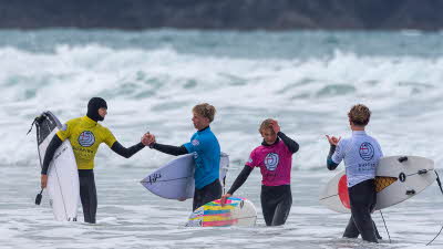 A group of young surfers congratulating each other stood in knee deep water with the white water waves behind
