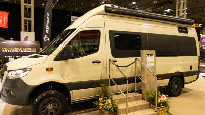 The RP Motorhomes Rebellion 2 is cream.  There are three steps with rails to gain easy access.  Next to the steps are two flower arrangements and there is an information board too. 