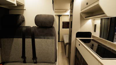 The Ace Motorhomes 1200 RL has mid and dark brown upholstery, the kitchen unit is to the right with an overhead cabinet.  There is a rear lounge.