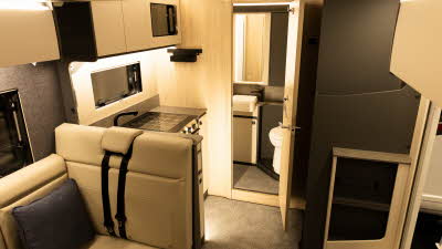 The Auto-Trail F-Line F60 has cream upholstery.  The kitchen is in the centre and to the rear is the washroom, the toilet and wash basin can be seen through the open door.
