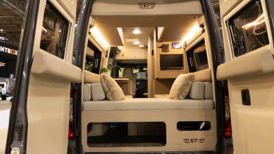 The RP Motorhomes Rebel U has caramel and cream u shaped sofas with two matching cushions in the corners.  The TV is to the right.  Its rear doors are open and there is storage under the sofa.