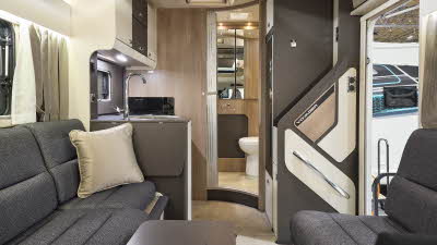 The Swift Voyager 540 has wooden flooring with dark grey upholstery, there is a gold cushion on the sofa.  The cabinets are dark brown and cream.  There is a step to the rear washroom.