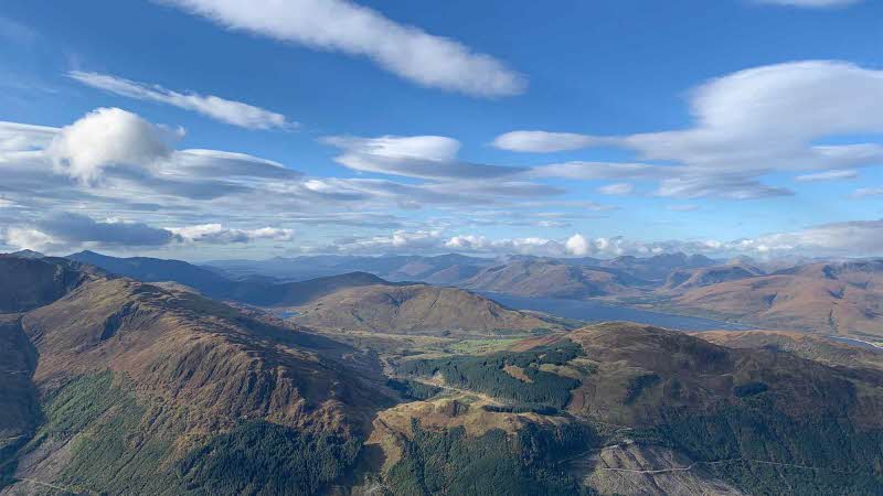 A view from Ben Nevis looking out over the mountains and munros below under a blue sky with white fluffy clouds
