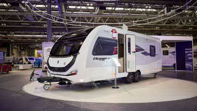 Swift Elegance Grande 860's exterior is white and grey with a large front window.  There are black graphics on the front panel.  The door is open and its corner steadies are down.  It has a twin axle. 