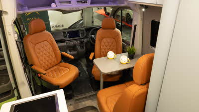The AURA 6EB's upholstery is orange leather.  There are white overhead lockers and the table has two mugs and a pot plant on it.