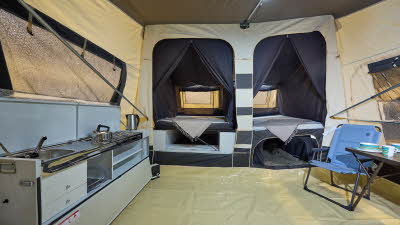 In the Jametic Outdoor AS there is a kitchen unit and a blue chair next to a table.  The bedroom doors are open.  There is lighting on the ceiling.