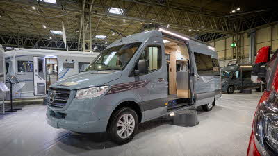 Auto-Sleeper M-Star's exterior is mid grey with black decals.  The sliding door is open revealing the kitchen and there is a step to gain easy access.  