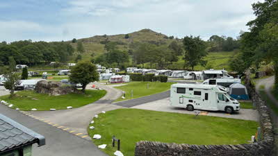 Looking out over the campsite with a motorhome on a pitch next to a grassy area, more motorhomes and caravans can be seen on pitches, with some green trees and a hill rising high in the distance