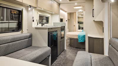 Interior of the Xplore XC QUAD with grey sofas, wood accents and grey carpets.  The large windows and roof light will let natural light flood in.  There is a fixed island bed and just beyond, the door to the washroom is open.