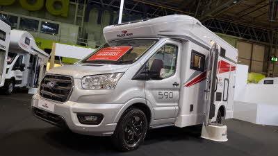 The Roller Team Kronos Compact 590 has a silver cab and white body with grey and red decals.  There is a white step outside the open habitation door. 