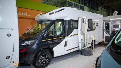 Benimar Mileo 243 Auto’s exterior has a dark blue cab and with its body being white with black, grey and yellow decals.  The entrance door is open and there is a step to gain easy access.  There is an information stand next to the step. 