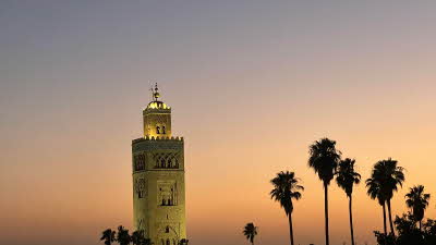 Minaret gently lit at sunset surrounded by palm trees