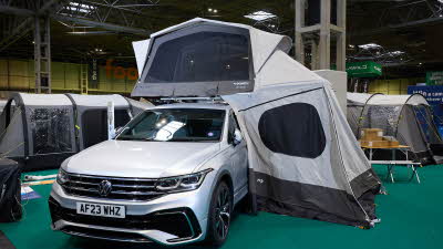 The Dometic TRT 140 AIR is displayed on a silver Volkswagen.  It has grey and white canvas and has an annex to the side of the vehicle.
