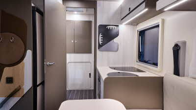 The Rimor Kilig 67 Plus has a wooden floor.  The upholstery is cream.  The cabinets are all very pale wood and the cupboard doors are a dark brown.  The interior door is open revealing two further large cupboards.