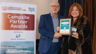 A Caravan and Motorhome Overseas Campsites Award Winner with the Chairman next to a sign showing Campsite Partner Awards, with Irish Ferries below it