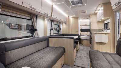 Interior of the Elddis Avanté APEX 840 with dark grey sofas, wood accents and grey carpets.  The large roof light will let natural light flood in.  There is a dinette opposite the kitchen.