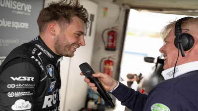 Man wearing motor racing jacket being interview by man with microphone