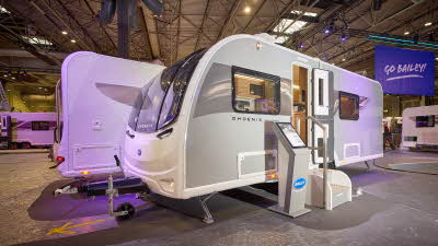 The Bailey Phoenix Black 642 has a grey exterior and a brown decal with light ripples on it.  The entrance door is open and there are two metal steps to gain easy access to the interior.  Next to the steps is an interactive stand.