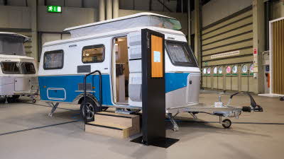 Eriba Touring 540 Harbour Blue Edition’s exterior is blue and white.  It’s pop top roof is extended.  There are two wooden steps to gain easy access and there’s a large interactive screen to the right.