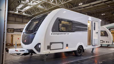 Swift Conqueror 480 is white with black patterned decals and a black front panel.  Its corner steadies are down and its entrance door is open.