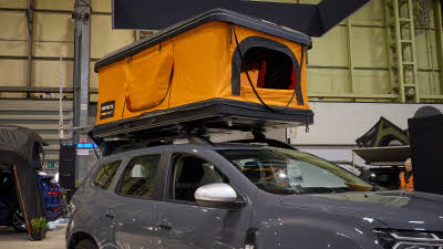 TentBox Classic 2.0 has orange canvas and a hard top and base.  Its window is open.  It is shown on the roof rack of a vehicle.