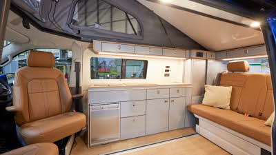 Ecowagon Expo+ has tan leather upholstery, silver kitchen units and a fridge. It has a wooden effect floor and there is a sliding rail to move the rear travels seats backwards or forwards easily. 