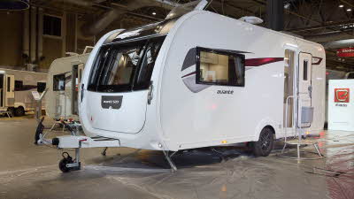 Elddis Avanté 520’s exterior is white with a grey and dark red patterned decal from the front to the rear.  The entrance door is open and there is a large metal step to gain easy access.  The roof light is open.  There is a TV aerial on the roof.