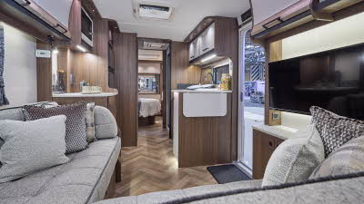 Interior of the Coachman Laser 855 Xtra with grey sofas, cosy cushions and wood accents and parquet effect flooring.  The door to the rear bedroom is open.  Perfect for relaxation and designed for comfort.
