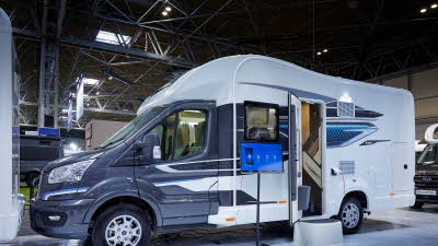 Swift Voyager 540, the vehicle has a grey cab and a predominantly white body, its habitation door is open showing into the interior, with a step to gain easy access.  There is an interactive screen outside the Voyager..
