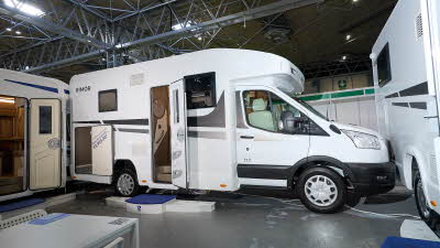 Rimor Kilig 67 Plus’ exterior has white body with grey and silver decals.  The habitation door is open and also the rear garage door.  There are three steps to gain easy access.