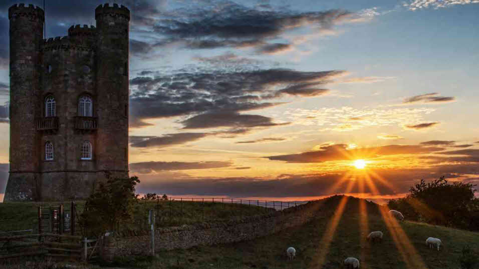 Sun setting on Broadway Tower and field of sheep