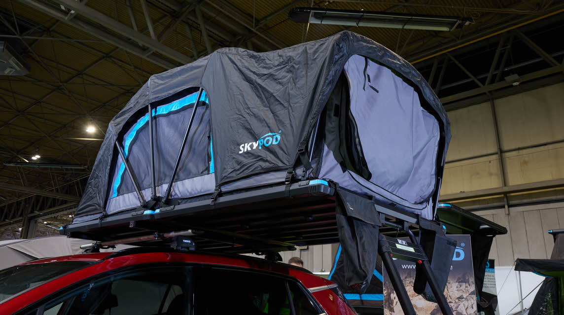 The SkyPod Lite has black canvas walls and has turquoise flashes around it.  The interior canvas is pale blue.  There are three support rods by the window.  There is a black ladder.