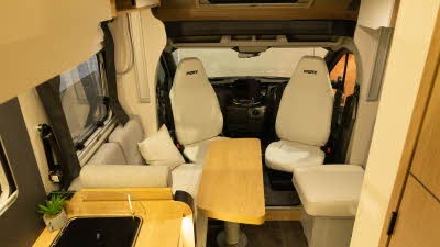 The Pilote Atlas A630G has light grey upholstery, the two front seats are swivelled to face in the van.  These are positioned around the wooden table with a bench and stool.  The floor is a grey tile effect.