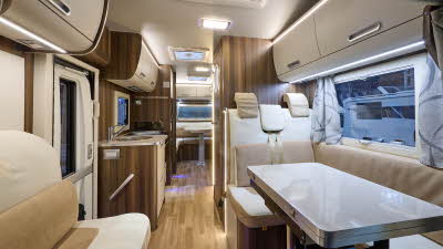 Rimor Super Brig Suite’s interior has cream and beige upholstery.  Its furniture is dark wood with cream doors.  At the rear there is a further lounge.  The front lounge’s table is folded and can be extended.  